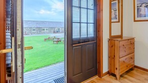 A room with a wooden door leading to a patio with a lawn and picnic tables.