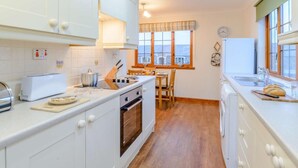 A compact kitchen with white cabinets, a stove, a toaster, and a window with a view.
