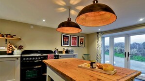 A kitchen with a wooden island, a stove, and hanging copper pendant lights. - 3 Bed in Tyn Y Groes (oc-80476) (Ty'n-y-groes)