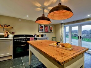 A kitchen with a wooden island, a stove, and hanging copper pendant lights. - 3 Bed in Tyn Y Groes (oc-80476) (Ty'n-y-groes)