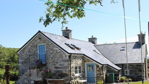 A stone house with a blue door, a small porch, and a swing set. - 3 Bed in Tyn Y Groes (oc-80476) (Ty'n-y-groes)