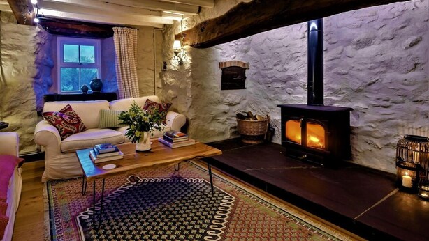 A cozy living room with a stone wall, a fireplace, a sofa, and a coffee table. - 3 Bed in Tyn Y Groes (oc-80476) (Ty'n-y-groes)
