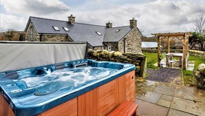 A hot tub in a garden with stone buildings in the background. - 3 Bed in Tyn Y Groes (oc-80476) (Ty'n-y-groes)