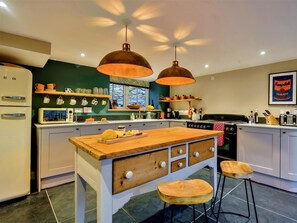 A kitchen with a central island, two pendant lights, a refrigerator, and a stove. - 3 Bed in Tyn Y Groes (oc-80476) (Ty'n-y-groes)