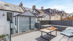 A rooftop deck with a table set for a meal, a seating area, and a view of neighboring buildings. - 2 Bed in Brixham (oc-80453) (Brixham)