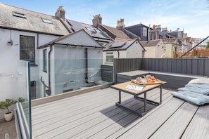 A rooftop deck with a table set for a meal, a seating area, and a view of neighboring buildings. - 2 Bed in Brixham (oc-80453) (Brixham)