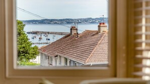 A view through a window of a building with a tiled roof, a chimney, and a satellite dish. - 2 Bed in Brixham (oc-80453) (Brixham)