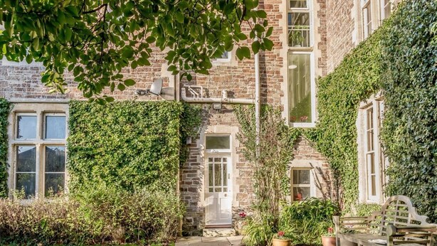 A stone building with ivy-covered walls, a paved courtyard, and a bench. - 2 Bed in Bideford (oc-80350) (Northam)