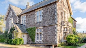 A stone building with a gabled roof, multiple windows, and a front door. - 2 Bed in Bideford (oc-80350) (Northam)
