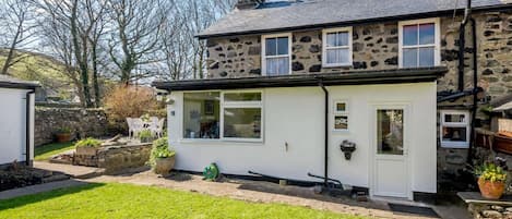 Une maison en pierre avec une extension blanche, un jardin et un ciel dégagé.
