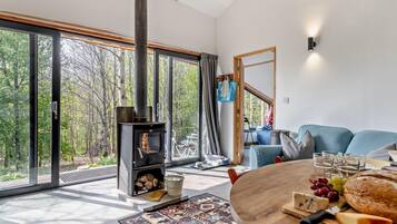 Un salon moderne avec une grande fenêtre, une cheminée, une table ronde en bois sur laquelle se trouve de la nourriture, et un canapé bleu.