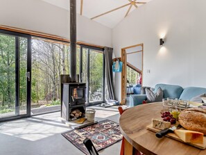 Un salon moderne avec une grande fenêtre, une cheminée, une table ronde en bois sur laquelle se trouve de la nourriture, et un canapé bleu.