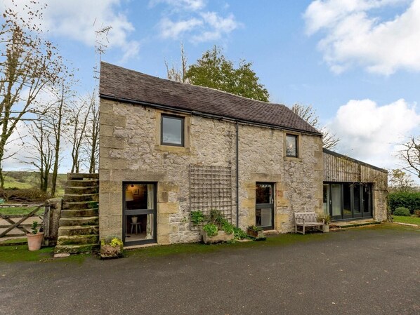 A stone building with a tiled roof, a wooden bench outside, and a paved driveway.