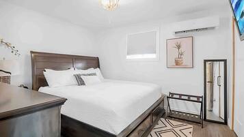 Una camera da letto con un letto, un comodino, una lampada, un condizionatore d'aria, un quadro incorniciato e una porta.