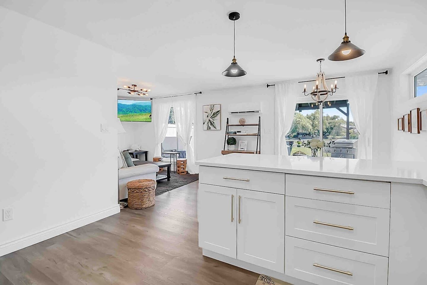 A modern kitchen with white cabinetry, pendant lighting, and a view of the outdoors.