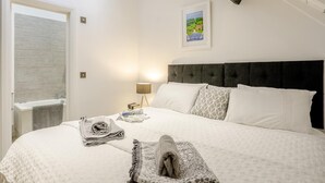 Uma cama bem arrumada com cabeceira, luminária de cabeceira, quadro na parede e janela com vista.