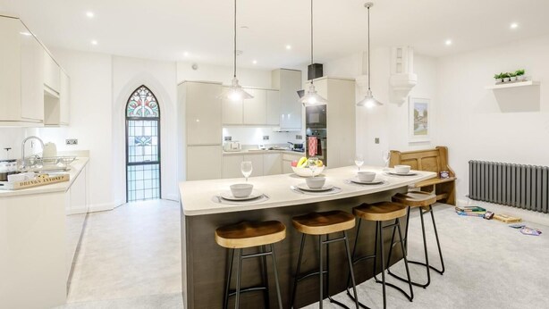 Uma cozinha moderna com uma ilha central, banquetas, luminárias pendentes e uma janela de vitral.