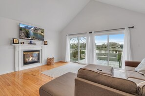 Ein Wohnzimmer mit Kamin, großem Fernseher, einer Couch und einem Balkon mit Blick.