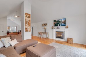 A living room with a fireplace, a sofa, a coffee table, and a dining area with a chair and table. - The Grand River Retreat. Pool/ hot tub avail Sep (Belle River)