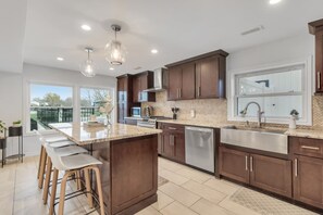 A modern kitchen with dark wood cabinets, a large island with bar stools, a stainless steel sink, and pendant lighting. - The Grand River Retreat. Pool/ hot tub avail Sep (Belle River)