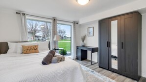 Um quarto com uma cama grande, uma escrivaninha, um guarda-roupa e vista para o exterior.