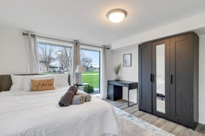 A bedroom with a large bed, a desk, a wardrobe, and a view of the outdoors. - The Grand River Retreat. Pool/ hot tub avail Sep (Belle River)