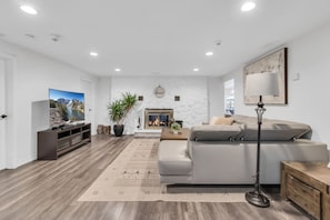 A modern living room with a fireplace, a flat-screen TV, a sofa, and a floor lamp. - Grand River Retreat: Pool, Hot Tub & Dock (Belle River)