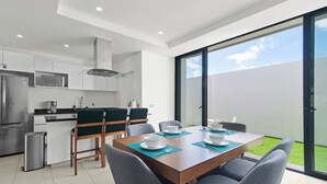 Cocina moderna con armarios blancos, refrigerador de acero inoxidable y comedor con mesa dispuesta para cuatro.
