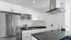 Una cocina moderna con armarios blancos, un refrigerador de acero inoxidable, un microondas y una encimera negra.