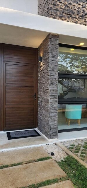 A modern building entrance with a stone pillar, a wooden door, and a glass window. - 2bd Tulum Country Club/PGA golf/Mid term/grocery (Tulum)