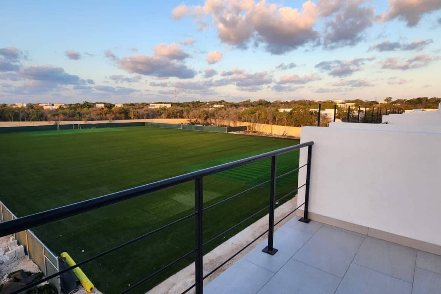 Terraço no telhado com gramado verde, parede branca e guarda-corpo de metal.