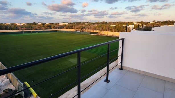 Una terraza en la azotea con césped, una pared blanca y barandilla de metal.