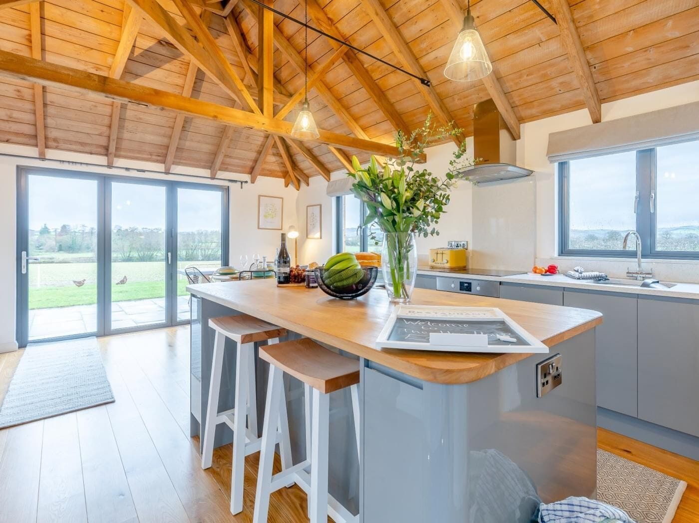 A modern kitchen with a large island, bar stools, a chalkboard, and a view of the outdoors.