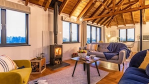 En hyggelig stue med brændeovn, sofa, stol og spiseområde med bord og stole.