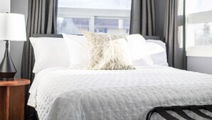 A neatly made bed with a white quilt, a patterned pillow, and a bedside lamp on a wooden nightstand.