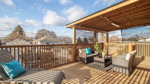 A wooden deck with outdoor furniture, a pergola, and a view of the neighborhood.