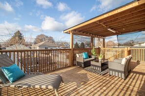 Une terrasse en bois, meublée pour l’extérieur, agrémentée d’une pergola et offrant une vue sur le quartier.