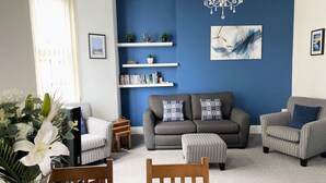 A living room with a sofa, armchairs, a dining table, and a chandelier. - 2 Bed in Tenby (oc-fb036) (Tenby)