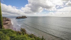 A coastal landscape with a rocky outcrop, beach, and calm sea under a partly cloudy sky. - 2 Bed in Tenby (oc-fb036) (Tenby)