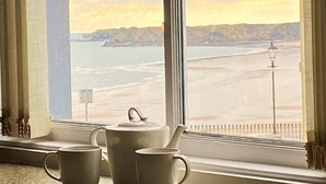 A room with a large window overlooking a beach, a kettle, and two cups on the windowsill. - 2 Bed in Tenby (oc-fb036) (Tenby)