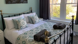 A bed with patterned bedding, a headboard, and a window with curtains. - 2 Bed in Tenby (oc-fb036) (Tenby)