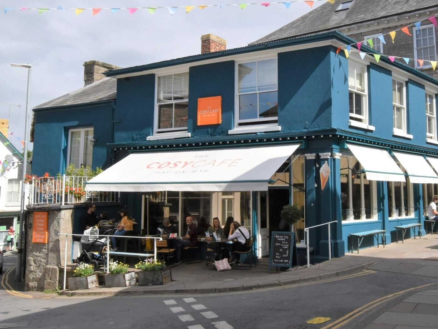 A blue building with a white awning labeled 'The Cosy Cafe.'