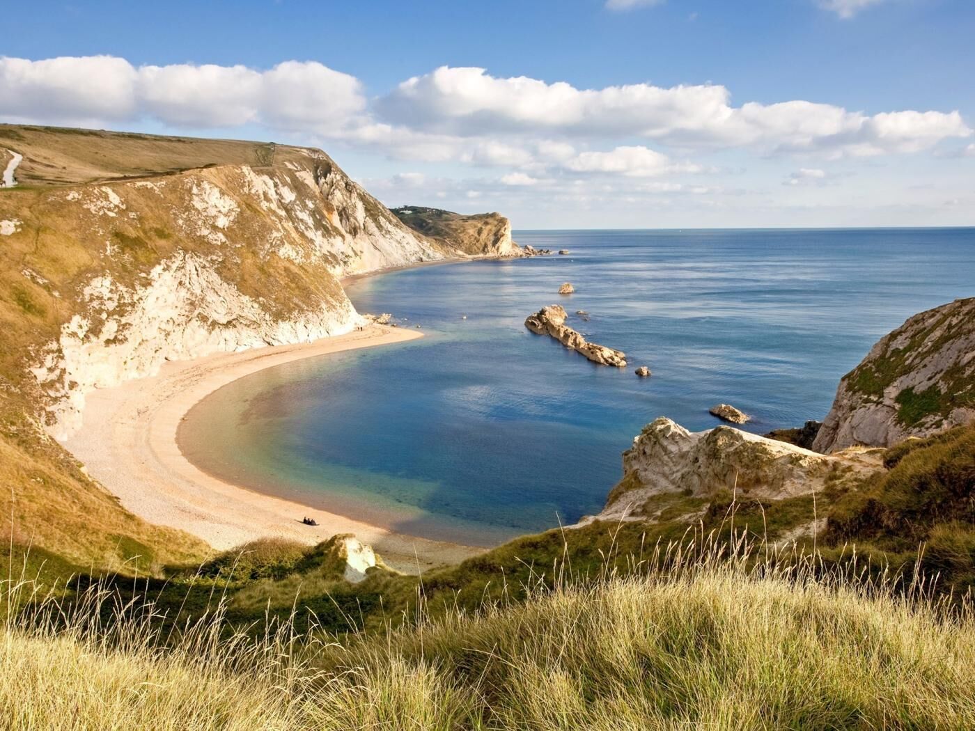 A coastal landscape with a sandy beach, cliffs, and calm sea.