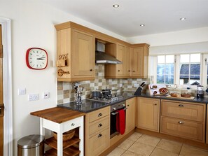 A kitchen with wooden cabinets, a stove, a sink, and a window with a view. - 5 Bed in Brecon (oc-bn318) (Bwlch)