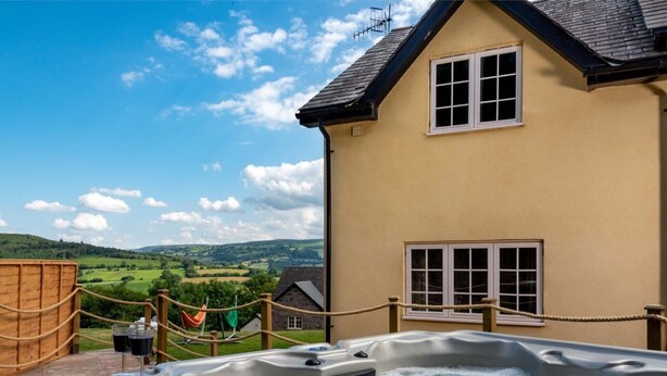Een jacuzzi in een achtertuin met uitzicht op een huis en glooiende heuvels.