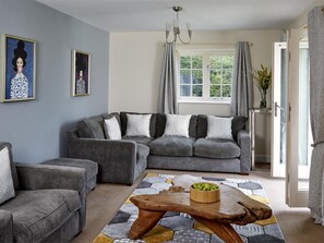 A living room with a grey sectional sofa, a wooden coffee table with apples, and a patterned rug. - 5 Bed in Brecon (oc-bn318) (Bwlch)