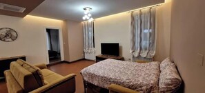 Una habitación con cama, sofá, televisor y ventana con cortinas.