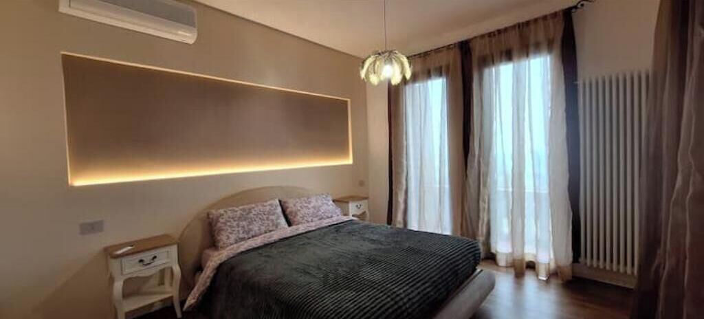 Un dormitorio moderno con una cama grande, mesitas de noche, una lámpara de pared y una ventana con cortinas.