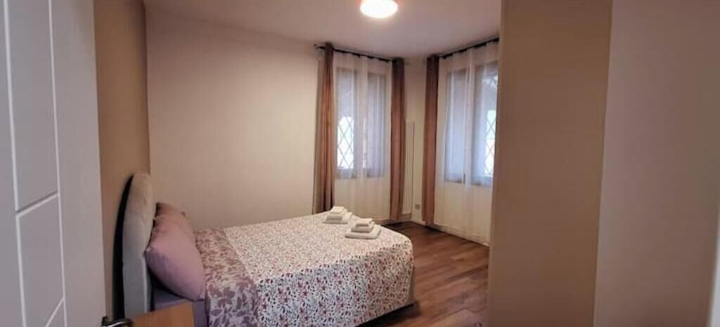 Une chambre à coucher avec un lit, une chaise et deux fenêtres avec des rideaux.