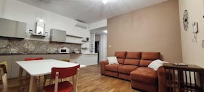 Una sala moderna con un sofá, una mesa de comedor con sillas, y una cocina con armarios y un microondas.